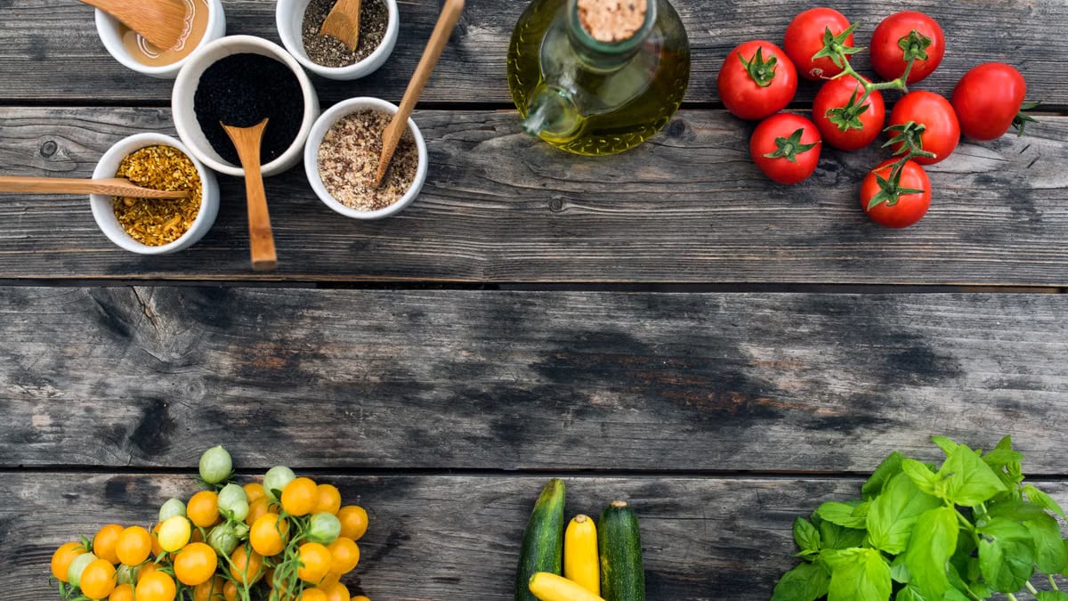 Top view of fresh vegetables and spices for salad placed on wooden table in daytime